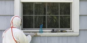 Man in full coverage hazard suit removing lead paint from windowsill